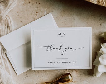 May include: A white thank you card with black text that reads "MIN thank you MADISON & NOAH SCOTT". The card is sitting on a light brown surface with a gold wax seal.