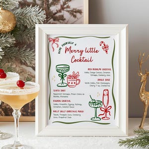 May include: A framed sign with the text "Have Yourself a Merry Little Cocktail" and cocktail recipes. Two cocktail glasses with sugared rims and a cherry garnish are in the foreground. A gold reindeer figurine is to the right.