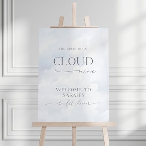 May include: A blue and white watercolor bridal shower sign with the text "The bride is on cloud nine. Welcome to Sarah's bridal shower."