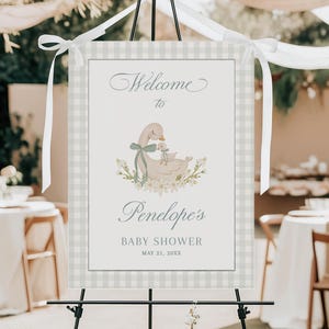 Könnte beinhalten: Willkommen zur Babyparty von Penelope Schild mit einem hellblauen und weißen Gingham-Hintergrund. In der Mitte befindet sich eine Aquarell-Illustration einer Mutterente und eines Entenküken. Der Text lautet "Willkommen zur Babyparty von Penelope 21. Mai 20XX".
