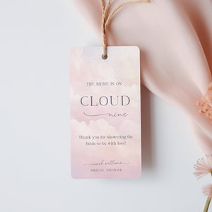 May include: A pink and white watercolor bridal shower favor tag with the text "The bride is on cloud nine" and "Thank you for showering the bride-to-be with love!"  The tag also includes the name "Sarah Williams" and the text "Bridal Shower".