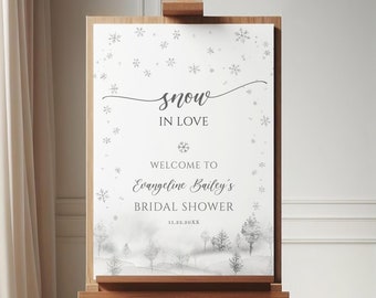 May include: A wooden easel supports a white sign with the text "snow in love" and "Welcome to Evangeline Bailey's Bridal Shower." The sign has a winter landscape illustration with snowflakes and trees. The date 11.23.20XX is also printed on the sign.