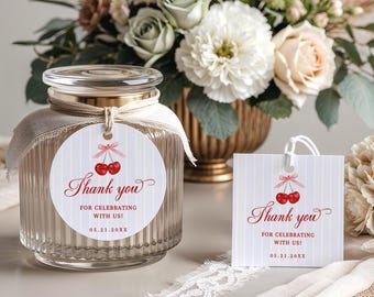 May include: A clear glass jar with a lid and a decorative tag that says "Thank you" with cherry illustrations. A matching gift bag is also present. The jar is tied with a ribbon and sits near a floral arrangement.