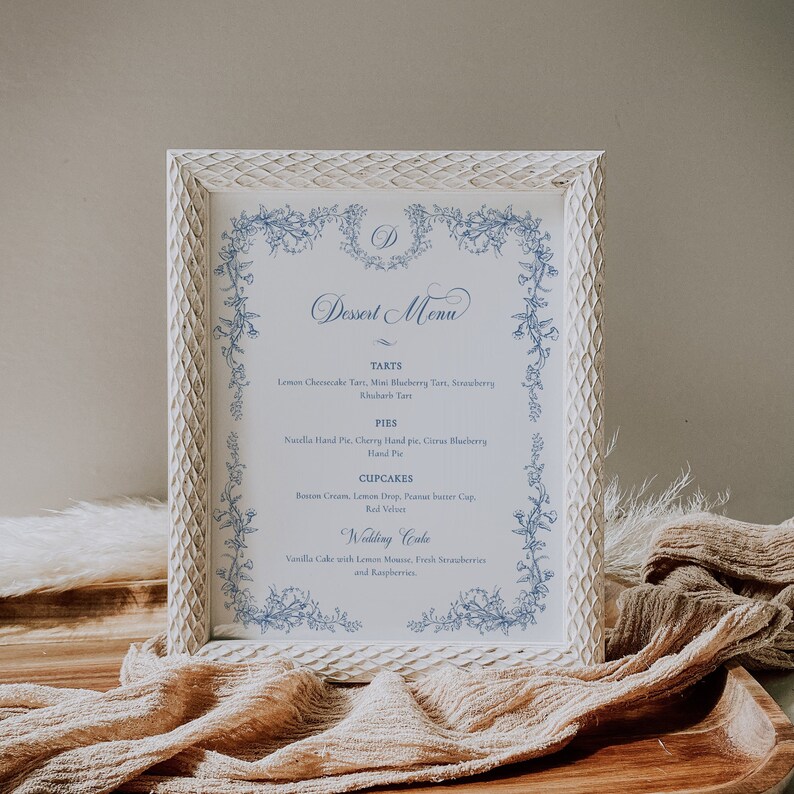 Puede incluir: Un men&uacute; de postres enmarcado en blanco con un borde floral azul y el texto "Dessert Menu" en cursiva. El men&uacute; enumera varios postres, incluyendo tartas, pasteles, cupcakes y un pastel de boda.