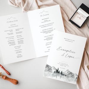 Könnte beinhalten: Ein Programm für eine Hochzeitszeremonie mit einem Aquarell-Design einer Berglandschaft. Das Programm enthält die Reihenfolge der Ereignisse, die Namen der Hochzeitsgesellschaft und die Namen der Braut und des Bräutigams: Evangeline & Logan.