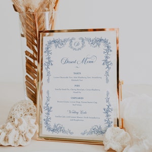 Puede incluir: Un men&uacute; de postres enmarcado en oro con un borde floral azul. El men&uacute; incluye tartas, pasteles, cupcakes y un pastel de boda con descripciones de cada art&iacute;culo.