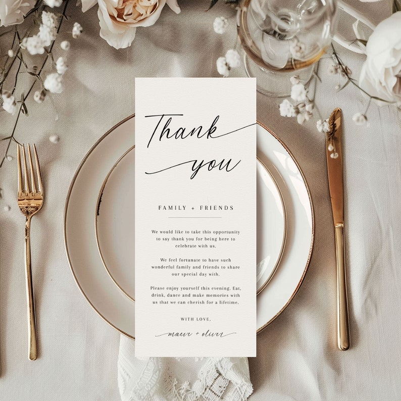 Pode incluir: Um cart&atilde;o de agradecimento retangular com uma escrita elegante, colocado em um prato branco com borda dourada. O cart&atilde;o diz "Thank you" acima de "Family + Friends" e uma mensagem de gratid&atilde;o. Um garfo e uma faca dourados est&atilde;o em ambos os lados.
