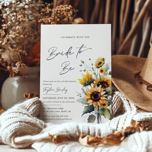 May include: A bridal shower invitation with the text "Bride to Be" and the name "Taylor Bailey". The invitation features a watercolor bouquet of sunflowers. The date is Saturday, July 20, 2024, at Sky Mountain Lodge.