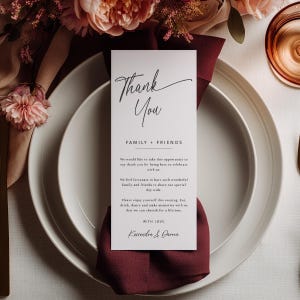 K&ouml;nnte beinhalten: Ein wei&szlig;es Gedeck mit einer weinroten Serviette und einer vertikalen Karte mit der Aufschrift "Thank You". Die Karte enth&auml;lt eine Nachricht an Familie und Freunde, mit den Namen Kassandra & Darren am unteren Rand. Blumengestecke und Glaswaren im Hintergrund.