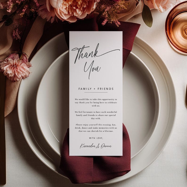 K&ouml;nnte beinhalten: Ein wei&szlig;es Gedeck mit einer weinroten Serviette und einer vertikalen Karte mit der Aufschrift "Thank You". Die Karte enth&auml;lt eine Nachricht an Familie und Freunde, mit den Namen Kassandra & Darren am unteren Rand. Blumengestecke und Glaswaren im Hintergrund.