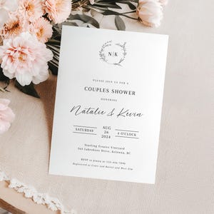 May include: A white wedding shower invitation with a floral wreath and the initials "N/K" in the center. The text reads "Please join us for a Couples Shower honoring Natalie & Kevin Saturday, Aug 26, 2024, 4 o'clock Starling Estates Vineyard, 363 Lakeshore Drive, Kelowna, BC RSVP to Jenna at 123-456-7890 Registered at Crate and Barrel and West Elm"