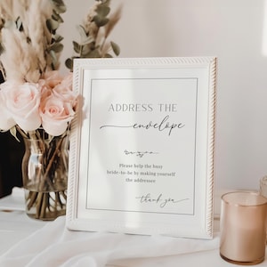 May include: A white framed sign with black text that reads "ADDRESS THE envelope Please help the busy bride-to-be by making yourself the addressee thank you".