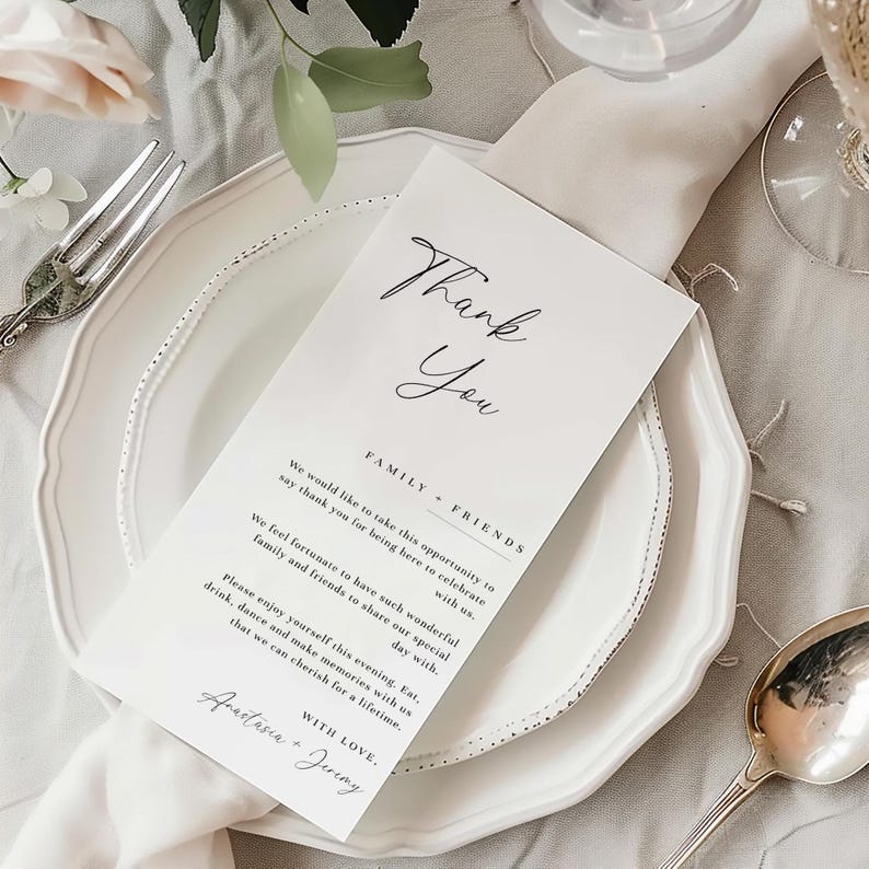 May include: A white place setting with a folded napkin, a fork, and a spoon. A white card with the words "Thank You" in elegant script is placed on the plate. The card also includes a message about celebrating with family and friends.