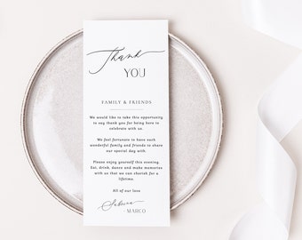 May include: A white card with elegant script that reads "Thank You" and a message to family and friends. The card is on a gray plate with a white ribbon in the background. The card's message is a thank you note.