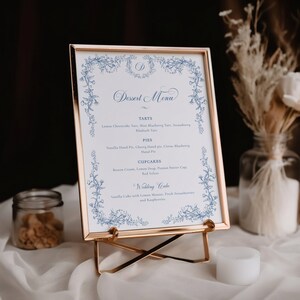 Puede incluir: Un men&uacute; blanco enmarcado con un borde floral azul y el texto "Dessert Menu" en cursiva azul. El men&uacute; enumera varios postres, incluyendo tartas, pasteles, cupcakes y un pastel de boda.