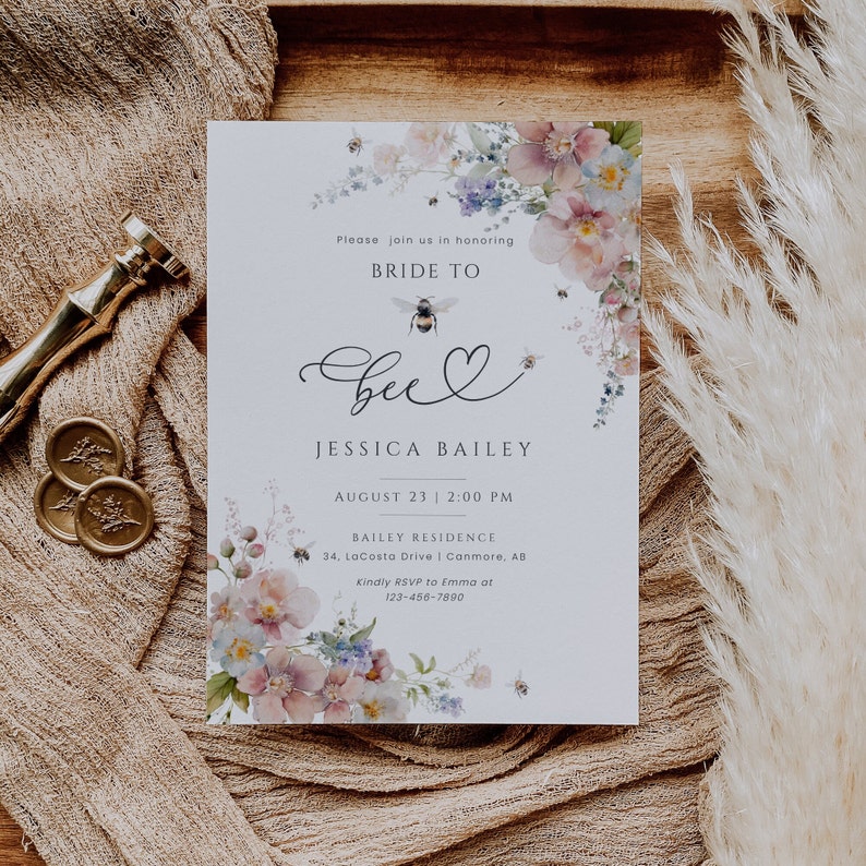 May include: A light blue bridal shower invitation with a watercolor floral design featuring pink and purple flowers, bees, and the text "Bride to Bee" with a heart. The invitation includes the bride's name, the date and time of the event, the location, and RSVP information.