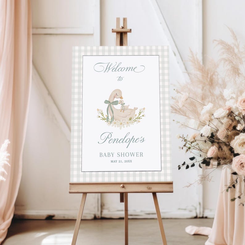 May include: A welcome sign for a baby shower with a gray and white gingham background. The sign features a watercolor illustration of a mother duck and her duckling. The text on the sign reads "Welcome to Penelope's Baby Shower May 21, 20XX".