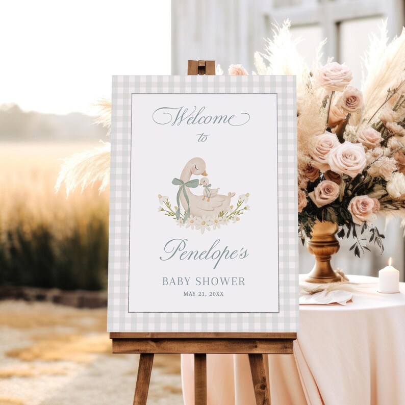 May include: A welcome sign for a baby shower with a gray and white gingham background. The sign features a watercolor illustration of a mother swan and baby swan with a green ribbon. The text on the sign reads "Welcome to Penelope's Baby Shower May 21, 20XX".