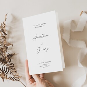 Könnte beinhalten: Eine Hochzeitsankündigungskarte mit dem Text "Willkommen zur Hochzeit von Anastasia & Jeremy" und dem Datum "26. August 20XX". Die Karte enthält auch den Ort der Hochzeit: "St. Vital Church, 1412 Thompson Street, Banff, AB."