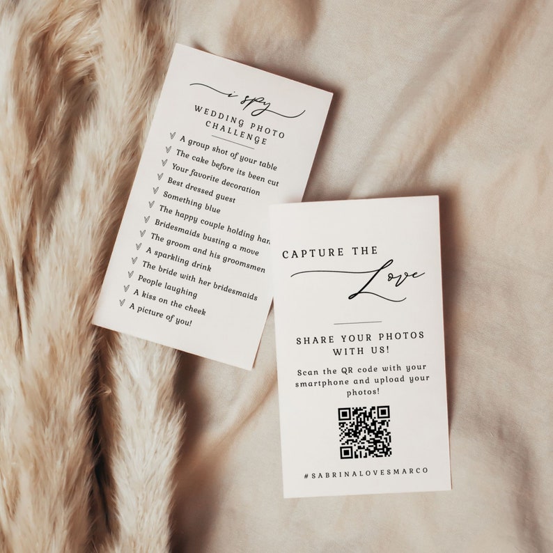 May include: Two white cards with black text. The first card has a list of items to find in wedding photos, titled "I Spy Wedding Photo Challenge". The second card has a QR code and the text "Capture the Love, Share Your Photos With Us! Scan the QR code with your smartphone and upload your photos! #SABRINALOVESMARCO".