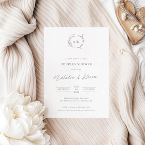 May include: A white wedding invitation with a floral wreath and the initials "NK" in the center. The text reads "Please join us for a Couples Shower honoring Natalie & Kevin Saturday Aug 26 4 O'Clock 2024 Starling Estates Vineyard 363 Lakeshore Drive, Kelowna, BC RSVP to Jenna at 123-456-7890 Registered at Crate and Barrel and West Elm"