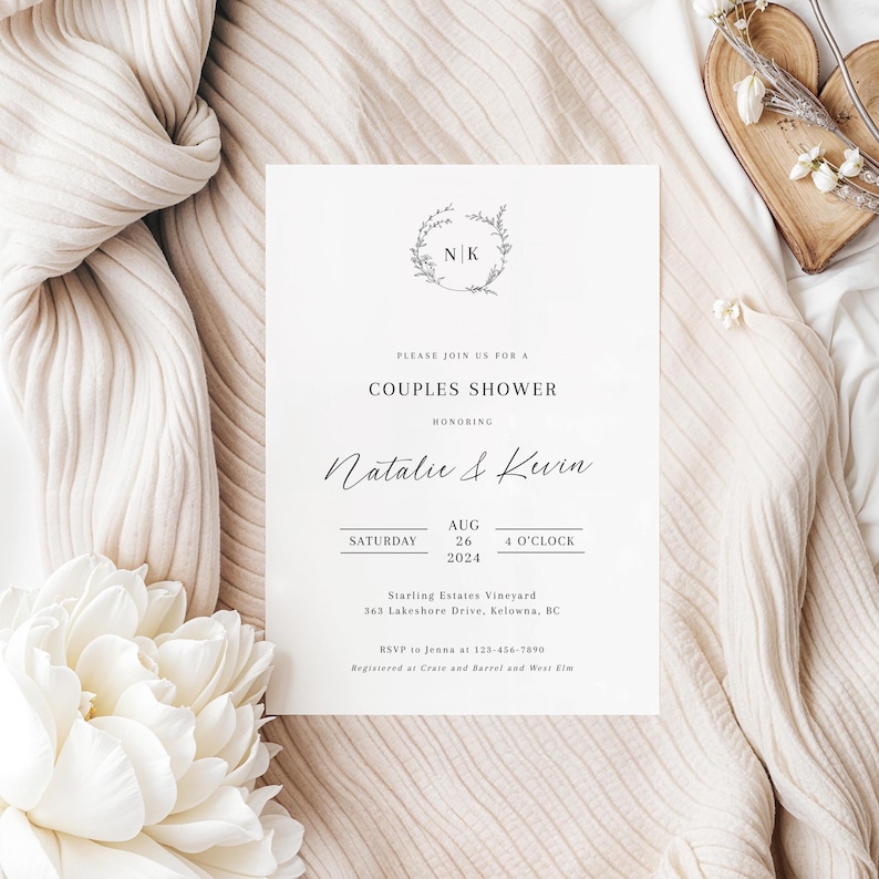 May include: A white wedding invitation with a floral wreath and the initials "NK" in the center. The text reads "Please join us for a Couples Shower honoring Natalie & Kevin Saturday Aug 26 4 O'Clock 2024 Starling Estates Vineyard 363 Lakeshore Drive, Kelowna, BC RSVP to Jenna at 123-456-7890 Registered at Crate and Barrel and West Elm"