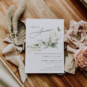 Peut inclure: Une carte d'invitation blanche avec des illustrations florales vertes et dor&eacute;es. Le texte indique "That's Amore" en &eacute;criture cursive. L'invitation est pour une f&ecirc;te pr&eacute;nuptiale de couple pour c&eacute;l&eacute;brer Sabrina & Marco le samedi 12 ao&ucirc;t 20XX &agrave; 16h00 &agrave; Bella Italia, 34 LaCesto Drive, Victoria, BC. Veuillez confirmer votre pr&eacute;sence aupr&egrave;s d'Amber au 123-456-7890.