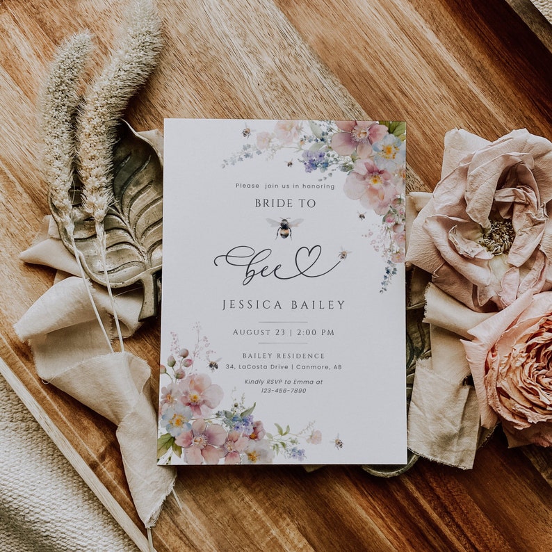 May include: A white bridal shower invitation with a watercolor floral design and a bee with a heart. The text reads "Please join us in honoring Bride to Bee Jessica Bailey August 23 | 2:00 PM Bailey Residence 34, LaCosta Drive | Canmore, AB Kindly RSVP to Emma at 123-456-7890"
