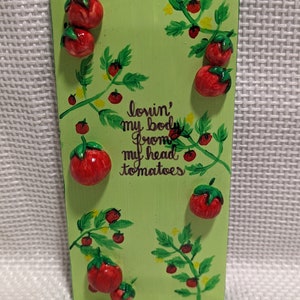 May include: A green wooden sign with a painted image of tomato vines and the text "lovin' my body from my head tomatoes".