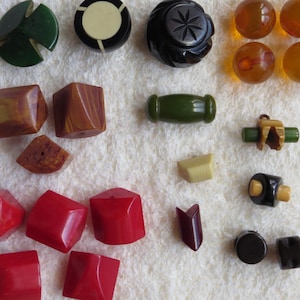 May include: A collection of vintage buttons in various shapes and colors. Includes green, black, red, and amber-colored buttons. Some are geometric, others are round or cylindrical. The buttons are made of different materials, including plastic and possibly Bakelite.