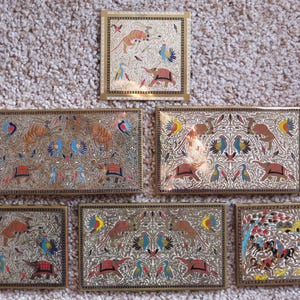 May include: Six small, rectangular brass boxes with intricate, colorful designs. Each box features a different scene with animals, birds, and floral patterns. The boxes are all made of brass and have a polished finish.