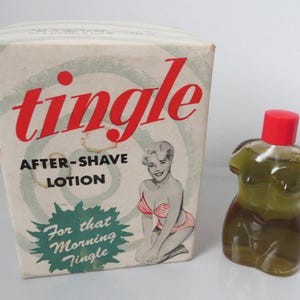 May include: Vintage "Tingle" after-shave lotion in a box with a pin-up girl illustration. The lotion bottle is shaped like a torso with a red cap. The box has the words "Tingle" and "After-Shave Lotion" in red and black.