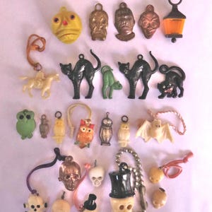 May include: A collection of vintage Halloween-themed charms and pendants in various shapes and colors. Includes black cats, skulls, owls, bats, and a lantern. Some charms are gold-toned, others are plastic. Perfect for jewelry making or crafting.