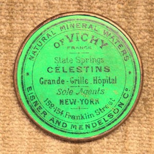 May include: A green and gold metal lid with black text that reads "Natural Mineral Waters of Vichy France State Springs Celestins Grande-Grille. Hopital Sole Agents New-York 152-154 Franklin Street * Eisner and Mendelson Co."