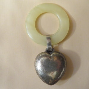 May include: A vintage baby rattle with a pale yellow plastic ring and a silver heart-shaped charm.