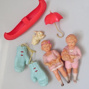 May include: A collection of vintage plastic toys in various colors. Includes a red canoe, a red umbrella, a cream-colored bunny, two light blue boxing gloves, and two dolls in pink outfits.