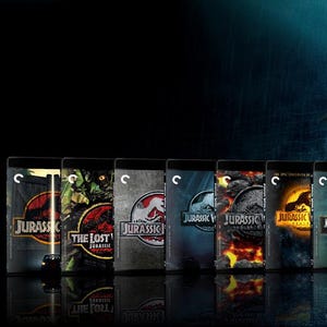 May include: A collection of Jurassic Park movie Blu-ray cases are displayed, showcasing various film titles. A large Tyrannosaurus Rex is featured in the background, with a person running away. The scene is set in a dark, rainy environment.