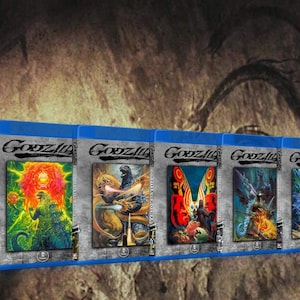 May include: A collection of Godzilla Blu-ray movie cases. Each case features unique artwork of the iconic monster in various action poses, with a blue case and the Godzilla logo at the top. The background is a textured, cave-like setting.