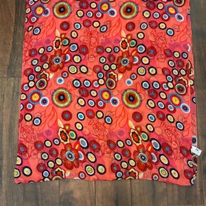 May include: A coral-colored scarf with a vibrant pattern of colorful circles and floral designs. The circles are in shades of red, yellow, blue, and green, creating a lively and eye-catching accessory. The scarf is made of a lightweight material.