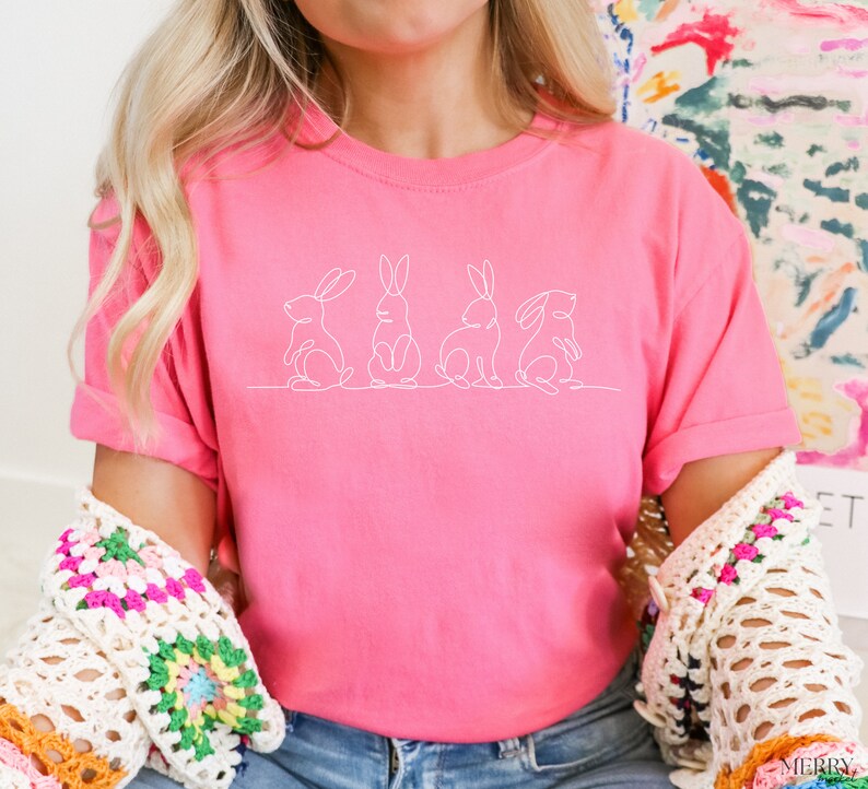 May include: A pink t-shirt with a white outline of five bunnies in a row.