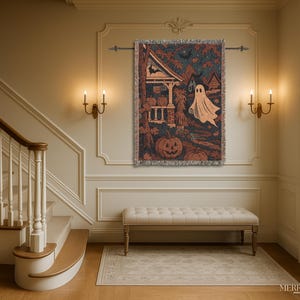 May include: A Halloween tapestry depicting a haunted house, pumpkins, and a ghost in shades of brown, orange, and blue. The tapestry has a fringed edge and is displayed on a wall above a bench in a room with warm lighting.
