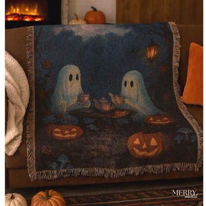 Peut inclure: Une couverture sur le thème d'Halloween avec deux fantômes de dessins animés prenant le thé avec des citrouilles sculptées. La couverture a un fond bleu foncé, une bordure à franges et une ambiance automnale.