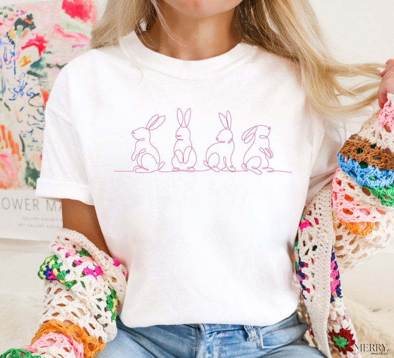 May include: White t-shirt with a pink line drawing of four bunnies in a row.