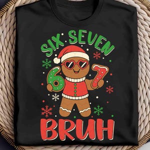 May include: Black t-shirt with a gingerbread man graphic wearing heart-shaped sunglasses and a Santa hat. The text reads "SIX SEVEN BRUH" in green and red, with snowflakes.