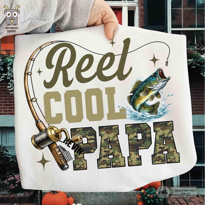 May include: White t-shirt with a fishing theme. The design includes a fishing rod, a leaping fish, and the words "Reel Cool Papa" in olive green and camouflage lettering. The shirt has a graphic design.