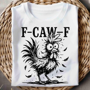 May include: White t-shirt with a black and white cartoon rooster graphic. The rooster has large eyes and feathers falling around it. The text "F-CAW-F" is printed above the rooster.