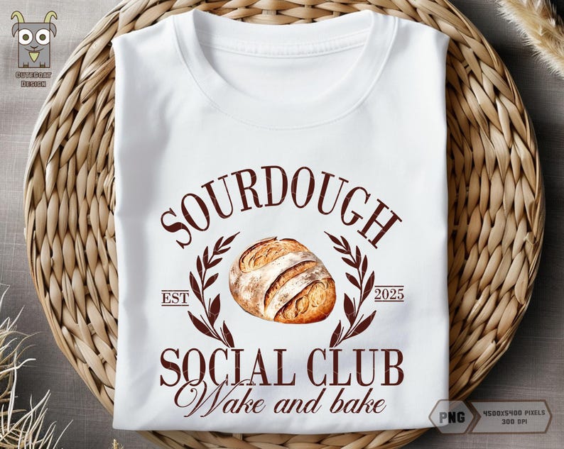 Op de afbeelding: Wit T-shirt met een bruin grafisch ontwerp met de tekst "Sourdough Social Club Wake and Bake" en een tekening van een zuurdesembrood. De tekst "Est 2025" is ook in het ontwerp opgenomen.
