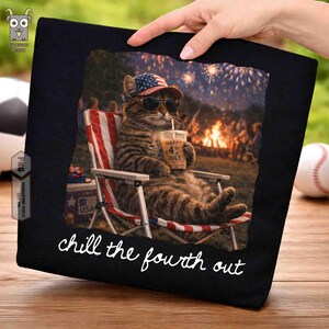 Puede incluir: Camiseta negra con un gato con gafas de sol y un sombrero patri&oacute;tico, relaj&aacute;ndose en una silla a rayas rojas, blancas y azules. El gato sostiene una bebida con el texto "Happy 4th of July". La frase "chill the fourth out" est&aacute; escrita en blanco.