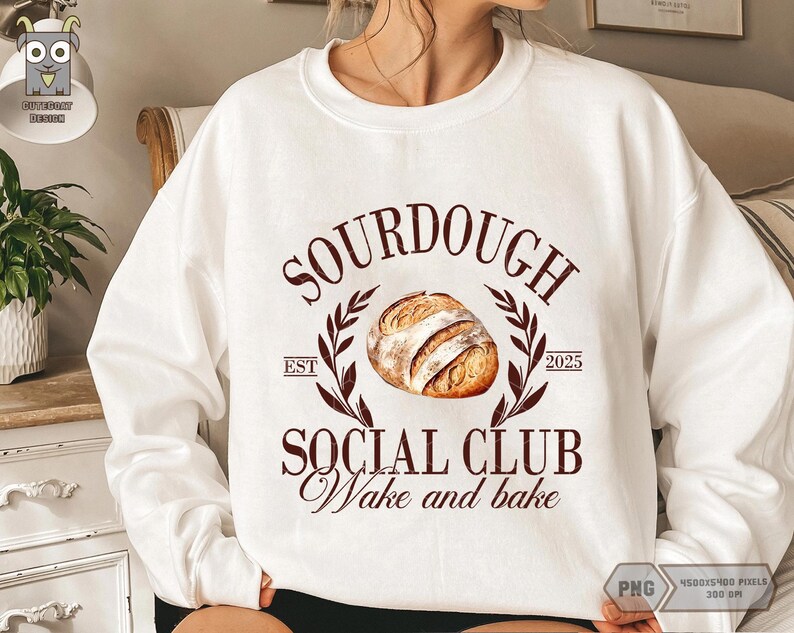 Op de afbeelding: Wit sweatshirt met een bruine afbeelding waarop "Sourdough Social Club Wake and Bake" staat, met een illustratie van een zuurdesembrood en de tekst "Est. 2025".