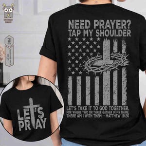 May include: Black t-shirt with the text "Need Prayer? Tap My Shoulder" above a distressed American flag design with a cross and crown of thorns. The front of the shirt says "Let's Pray" with a cross.